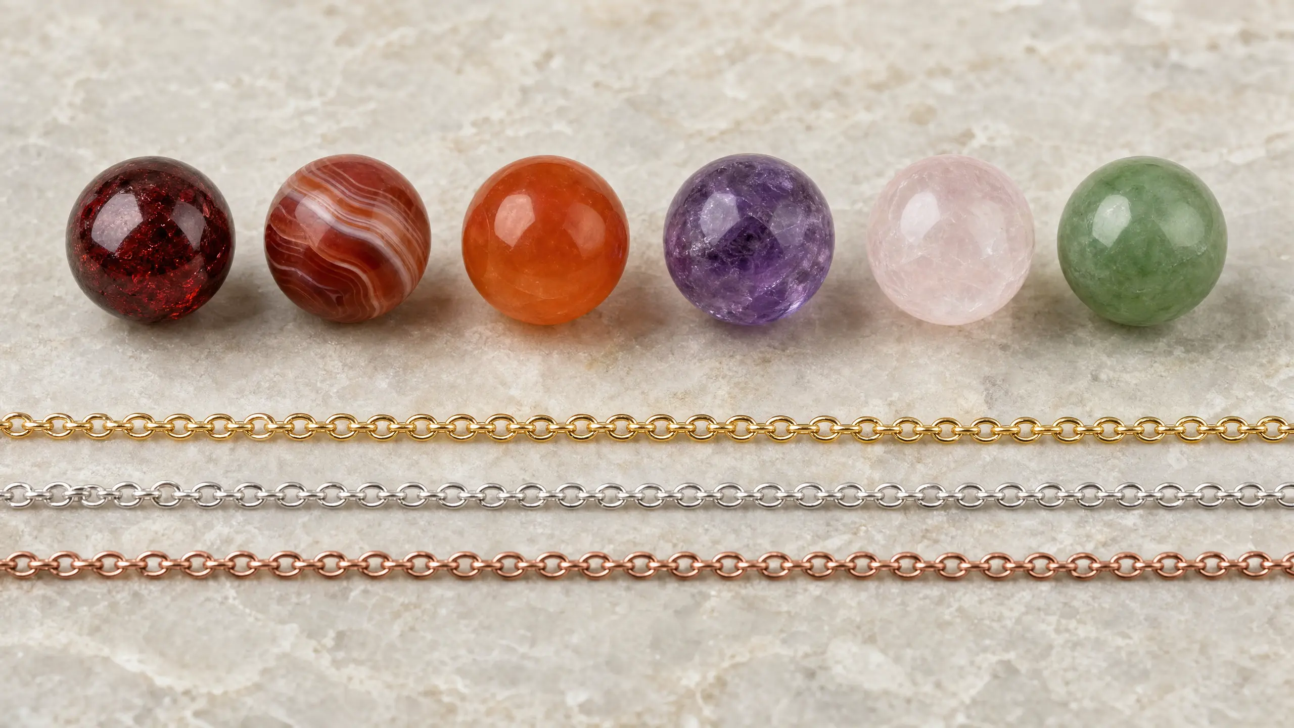 Row of polished garnet, red agate, carnelian, amethyst, rose quartz, and jade beads beside gold, silver, and copper chain