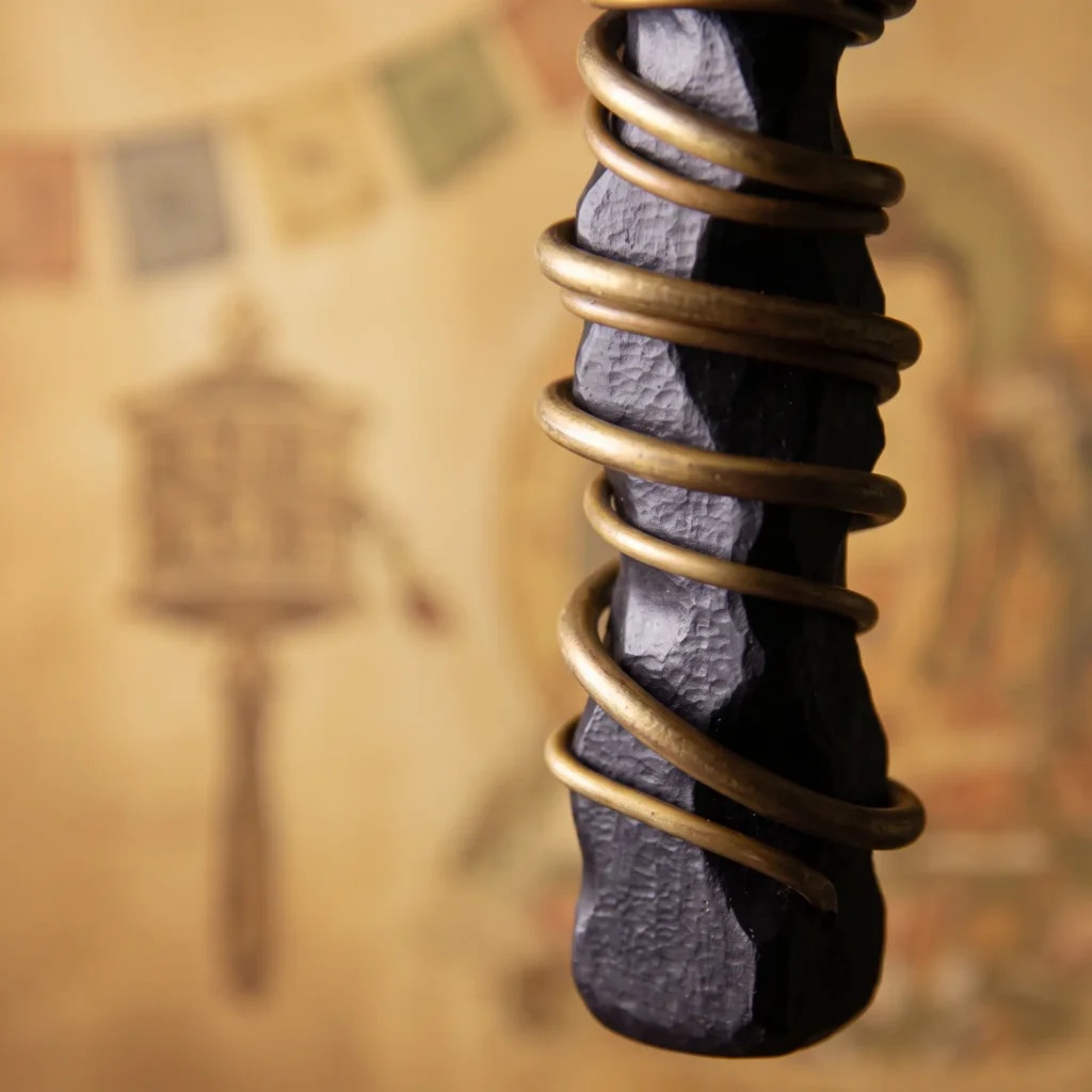 Hand-carved ebony wood pendant with a chisel-textured black surface and brass wire spiral, with Tibetan prayer flags behind