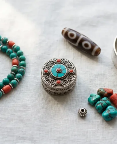 Flat lay of Tibetan Buddhist jewelry: turquoise and coral mala, silver ga'u amulet box, dzi bead and knot cuff