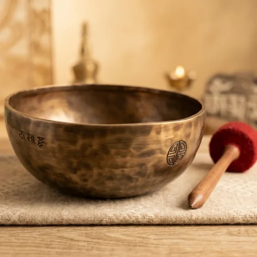 Hand-hammered Tibetan singing bowl with engraved mantra script and longevity symbol beside a red felt-tipped striker on a linen mat