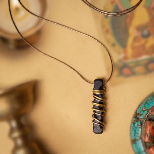 Unisex ebony wood and brass pendant necklace on a thin cord, with a Tibetan thangka and turquoise-coral ornament behind
